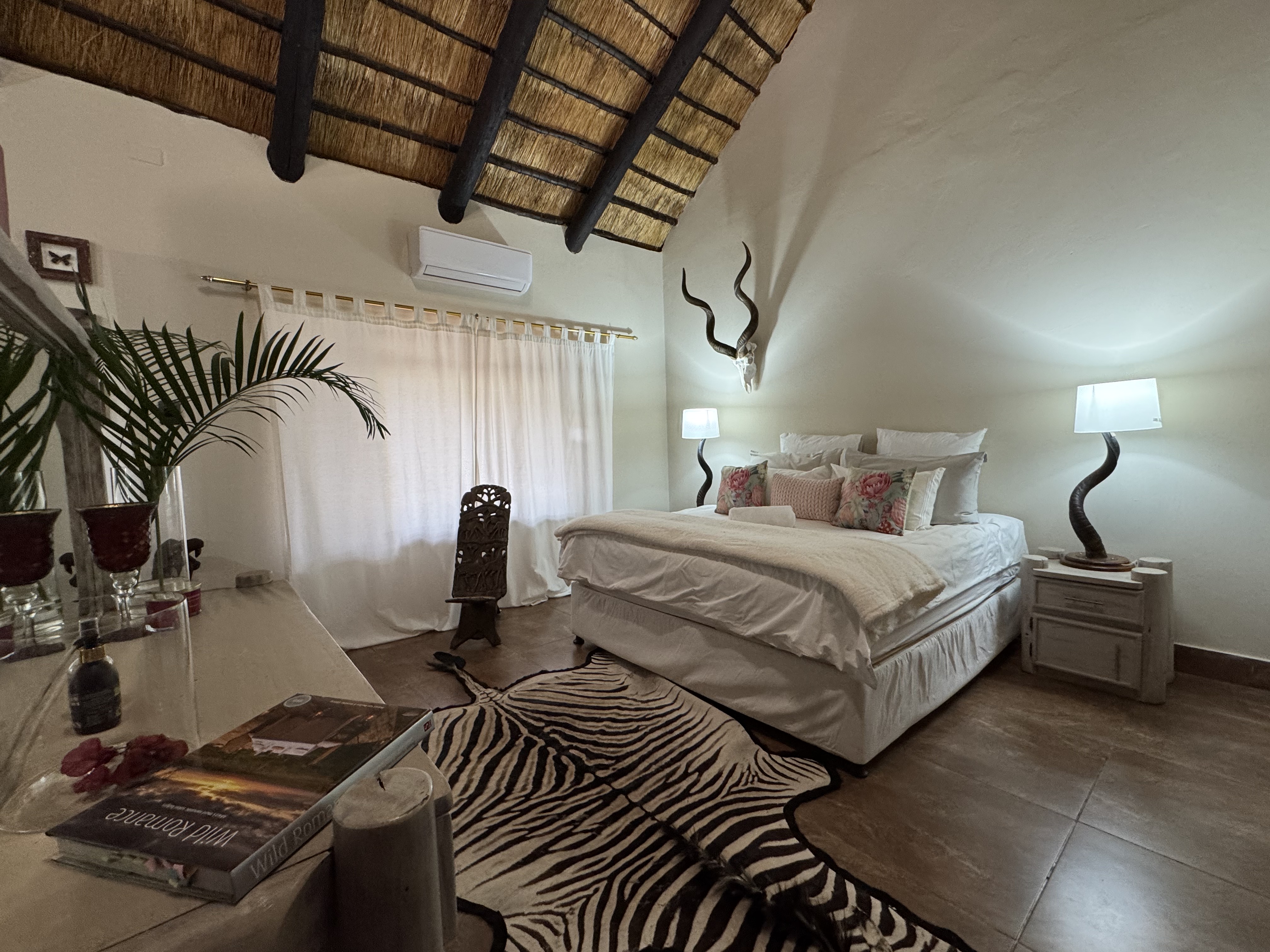 Thatched-roof JutLand suite with a king bed, kudu horns, and zebra rug