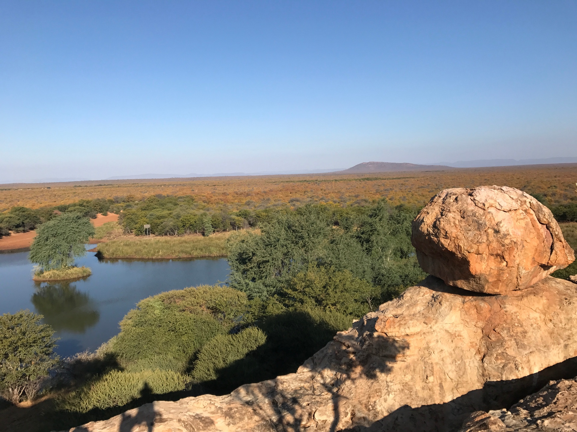 Panoramic bushveld vista with balanced boulder overlooking a waterhole